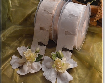 May include: Two spools of white satin ribbon with a decorative scalloped edge. The ribbon is wound around a clear plastic spool. The ribbon is decorated with a delicate floral pattern.