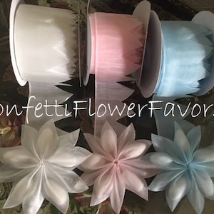 May include: Three spools of sheer ribbon in white, pink, and light blue. The ribbon is curled and has a scalloped edge. The ribbon is displayed on a white surface with the text "Confetti Flower Favors".
