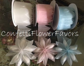 May include: Three spools of sheer ribbon in white, pink, and light blue. The ribbon is curled and has a scalloped edge. The ribbon is displayed on a white surface with the text "Confetti Flower Favors".