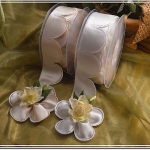 May include: Two spools of white satin ribbon with scalloped edges. The ribbon is on a light green background with two white fabric flowers.