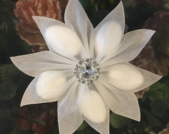 May include: A white tulle flower with a rhinestone centre. The flower is made of six petals and is perfect for adding a touch of elegance to any occasion.