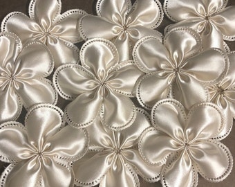 May include: A group of eight ivory satin flowers with scalloped edges and a pearl-like bead detail around the edges.