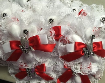 May include: White lace and satin fabric with red ribbon bows and silver charms. The charms feature a cross and a small flower design.