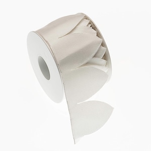 Puede incluir: Un rollo de cinta de color crema con un diseño de borde en forma de pétalo. La cinta está hecha de una tela texturizada y está parcialmente desenrollada, revelando las formas de pétalos. La bobina es blanca, sobre un fondo blanco.
