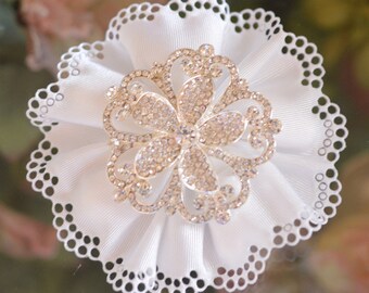 Könnte beinhalten: Eine weiße Stoffblume mit einem Strasssteinbesatz in der Mitte. Die Blume hat einen gewellten Rand und ist aus einem weichen, zarten Material gefertigt.