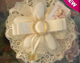 Könnte beinhalten: Eine weiße Satinblume mit einer Spitzenborte und einer mit Strass besetzten Schleife. Die Blume ist mit einem weißen Satinband gebunden und hat ein kleines Etikett mit der Aufschrift "Something for you".