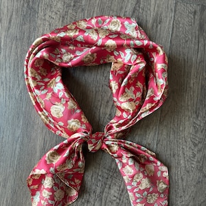 May include: A red bandana with a floral pattern featuring beige roses and green leaves.