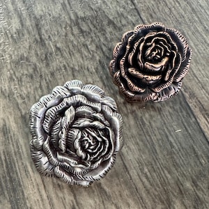 May include: Two decorative metal rose-shaped drawer pulls, one in silver and one in copper.