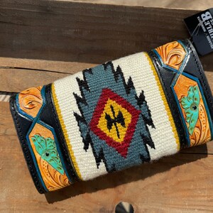 May include: A black leather wallet with a white, blue, red, and yellow geometric pattern. The wallet has a tooled leather design with a butterfly motif. The brand name "WILD HAGS DOUBLE B" is visible on a tag.