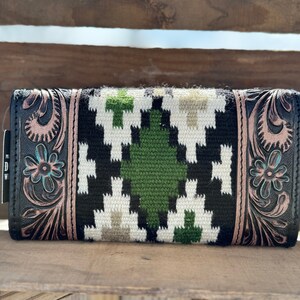 May include: Black leather wallet with a geometric pattern in white, green, and brown. The wallet has a floral design embossed on the sides.