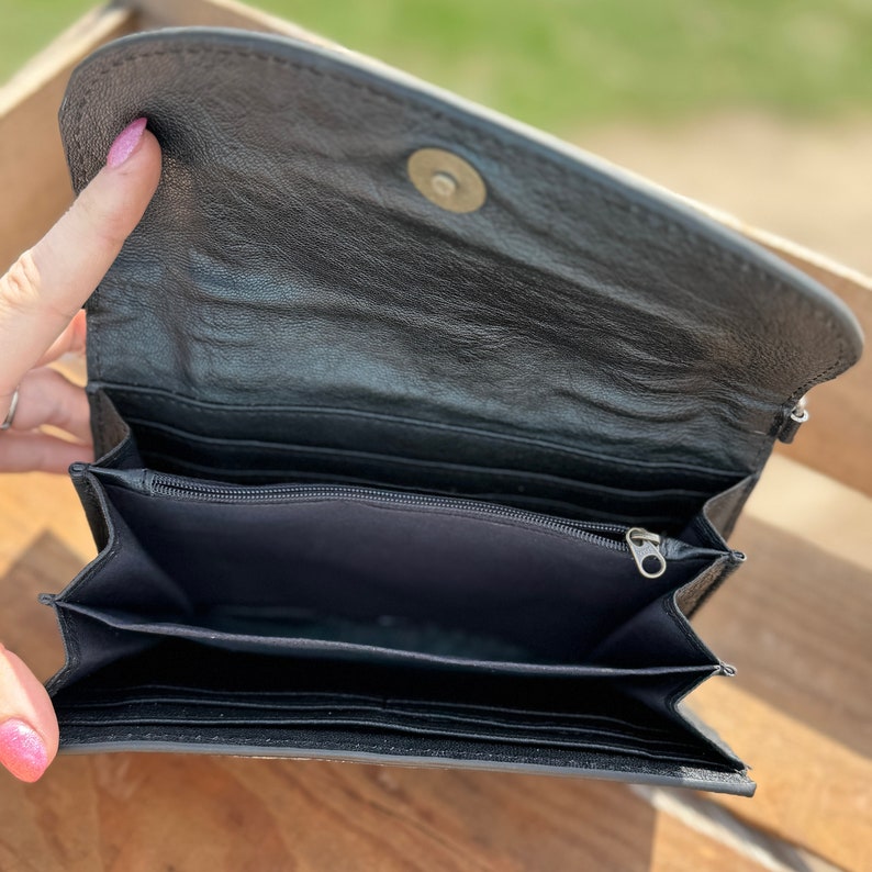 May include: Black leather wallet with multiple compartments and a zippered pocket. The wallet is open and empty.
