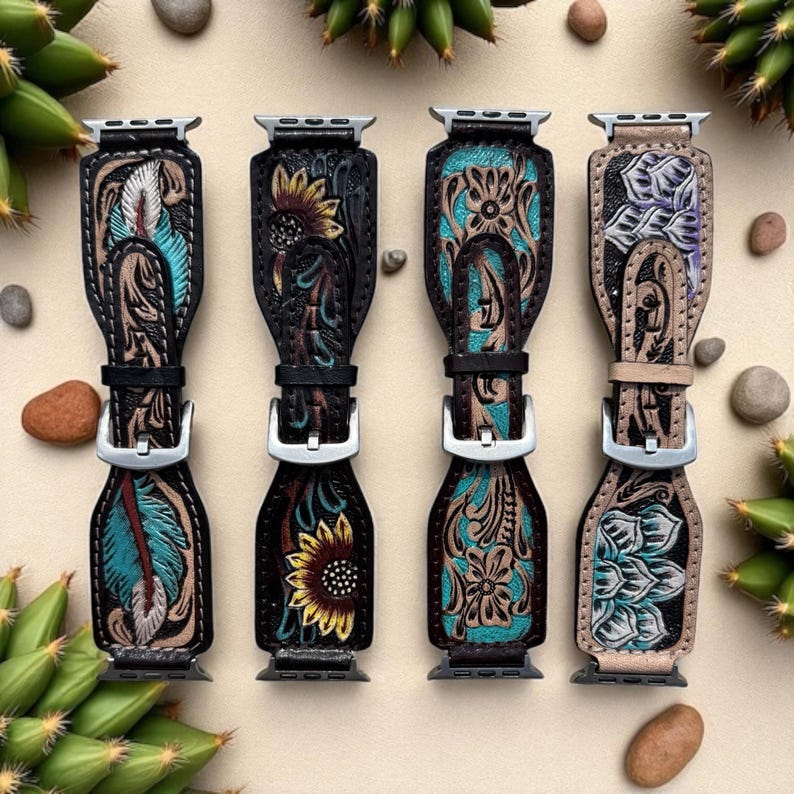 Puede incluir: Cuatro correas de reloj de cuero con intrincados dise&ntilde;os florales y de plumas. Cada correa presenta una combinaci&oacute;n de colores diferente, incluyendo turquesa, negro y beige, con hebillas plateadas. Las correas se exhiben sobre una superficie neutra con peque&ntilde;as piedras y vegetaci&oacute;n.