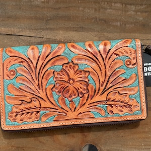 May include: A turquoise and brown leather wallet with a floral design. The wallet has a zip closure and a tag that reads "DOUBLE B WILD RAGS". The floral design is embossed on the leather.