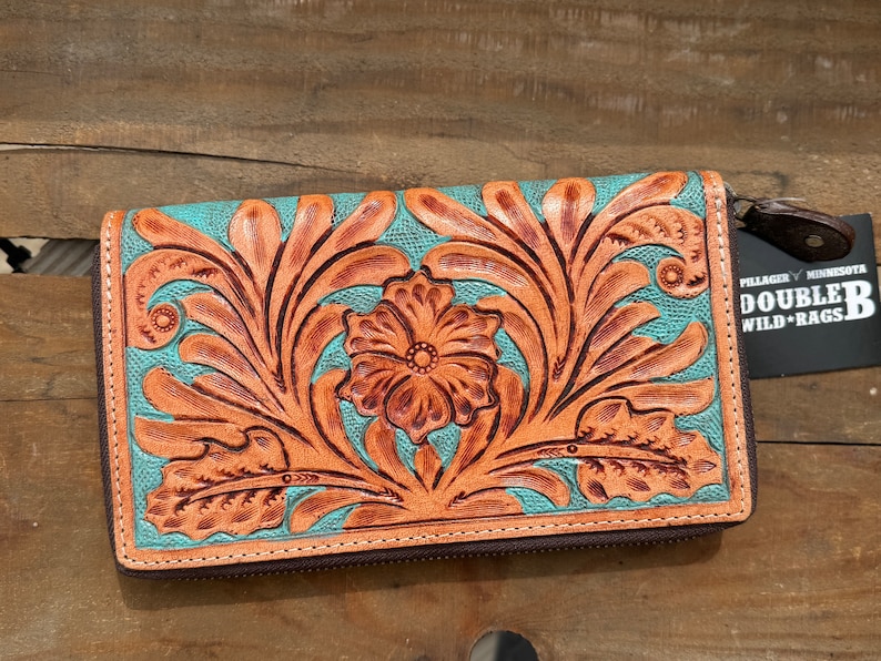 May include: A turquoise and brown leather wallet with a floral design. The wallet has a zip closure and a tag that reads "DOUBLE B WILD RAGS". The floral design is embossed on the leather.