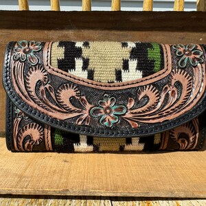 May include: A black leather wallet with a tooled floral design and a woven patterned flap. The wallet has a brown and green color scheme with turquoise accents. The wallet is labeled "Minnesota Saddle Bags".