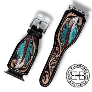 Puede incluir: Dos correas de reloj de cuero negro con dise&ntilde;o de pluma. Las plumas son turquesas, blancas y rojas, con detalles en beige y negro. Las correas tienen hebillas y conectores plateados. El logotipo de Wild Rags est&aacute; en la esquina inferior derecha.