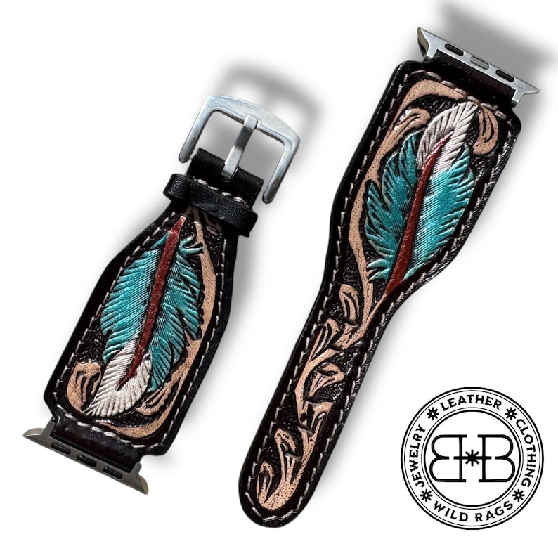 Puede incluir: Dos correas de reloj de cuero negro con dise&ntilde;o de pluma. Las plumas son turquesas, blancas y rojas, con detalles en beige y negro. Las correas tienen hebillas y conectores plateados. El logotipo de Wild Rags est&aacute; en la esquina inferior derecha.