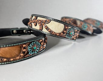 May include: Close-up of several decorative dog collars. The collars feature a black leather base with a light-colored fur center. They are adorned with copper-colored metal accents, turquoise-colored floral designs, and small copper studs.