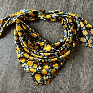 May include: A black and gold floral patterned bandana with a knotted design. The bandana is made of a silky material.