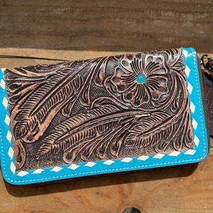 May include: A brown leather wallet with a floral and feather design. The wallet has a turquoise border with white stitching and a turquoise center stone in the flower. The wallet has a zipper closure and a tag that says "DOUBLE D RAGS D".
