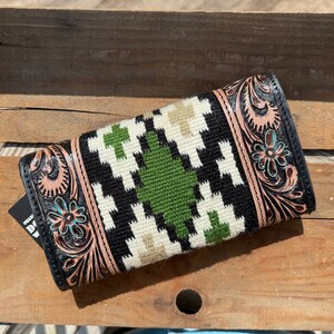 May include: A black leather wallet with a tooled floral design and a green, white, and black woven pattern. The wallet has a flap closure and a brown leather trim.
