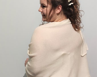 Puede incluir: Un chal de punto blanco con un borde festoneado. El chal está drapeado sobre los hombros de una persona con cabello castaño rizado y una corona de flores blancas.