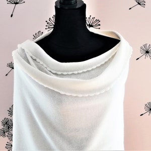 Puede incluir: Poncho blanco de punto con un borde festoneado. El poncho está drapeado sobre un maniquí negro.