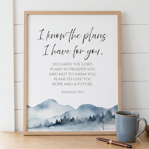 May include: A framed print with the text "I know the plans I have for you," and a watercolor mountain scene. The quote is from Jeremiah 29:11. A mug and pen are on the table.