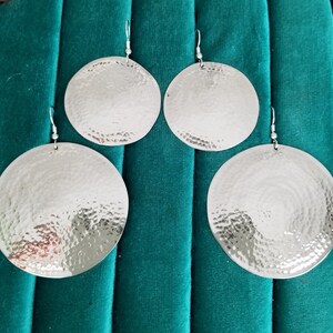 May include: Four silver earrings with a hammered texture. The earrings are round and have a shiny finish.