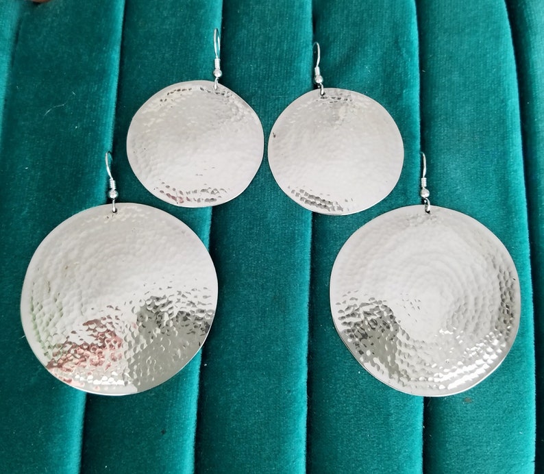 May include: Four silver earrings with a hammered texture. The earrings are round and have a shiny finish.