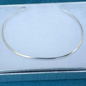 May include: A silver choker necklace in a white box with a silver lining.