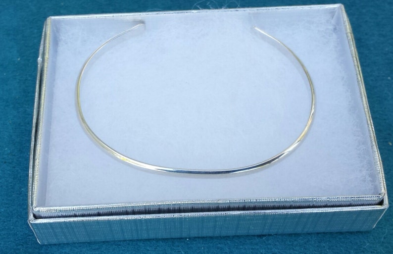 May include: A silver choker necklace in a white box with a silver lining.