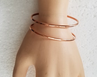 May include: Two rose gold hammered metal bangles stacked on a mannequin's wrist.