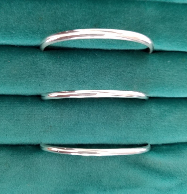 May include: Three silver bangle bracelets of varying sizes, stacked on a green velvet surface.