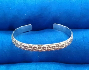 May include: A silver bracelet with a floral design. The bracelet is made of a thin metal band with a textured surface.