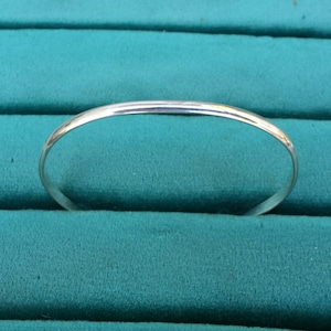 May include: A simple silver bangle bracelet, shown against a teal green background.