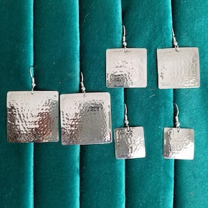 May include: Set of five silver square earrings with a hammered texture. The earrings are of varying sizes.