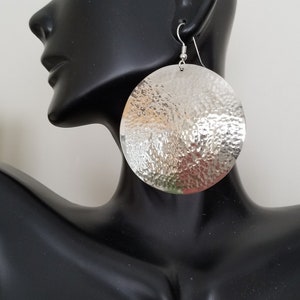 May include: Silver hammered round disc earrings. The earrings are large and have a textured surface.