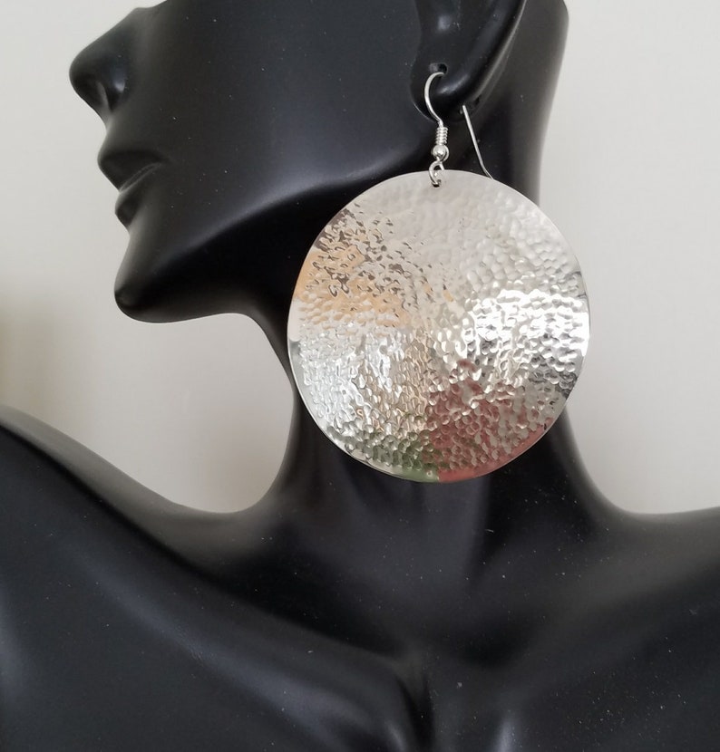 May include: Silver hammered round disc earrings. The earrings are large and have a textured surface.