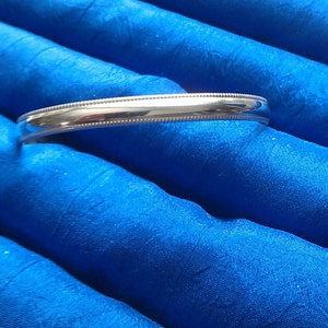 Pu&ograve; includere: Un braccialetto rigido in argento con un bordo perlato. Il braccialetto &egrave; su uno sfondo di tessuto blu.