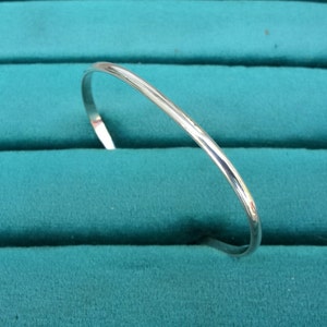 May include: A silver bangle bracelet with a smooth, polished finish. The bracelet is displayed on a teal velvet background.