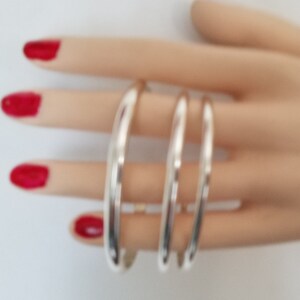 May include: Three silver bangle bracelets stacked on a hand. The bracelets are smooth and shiny.