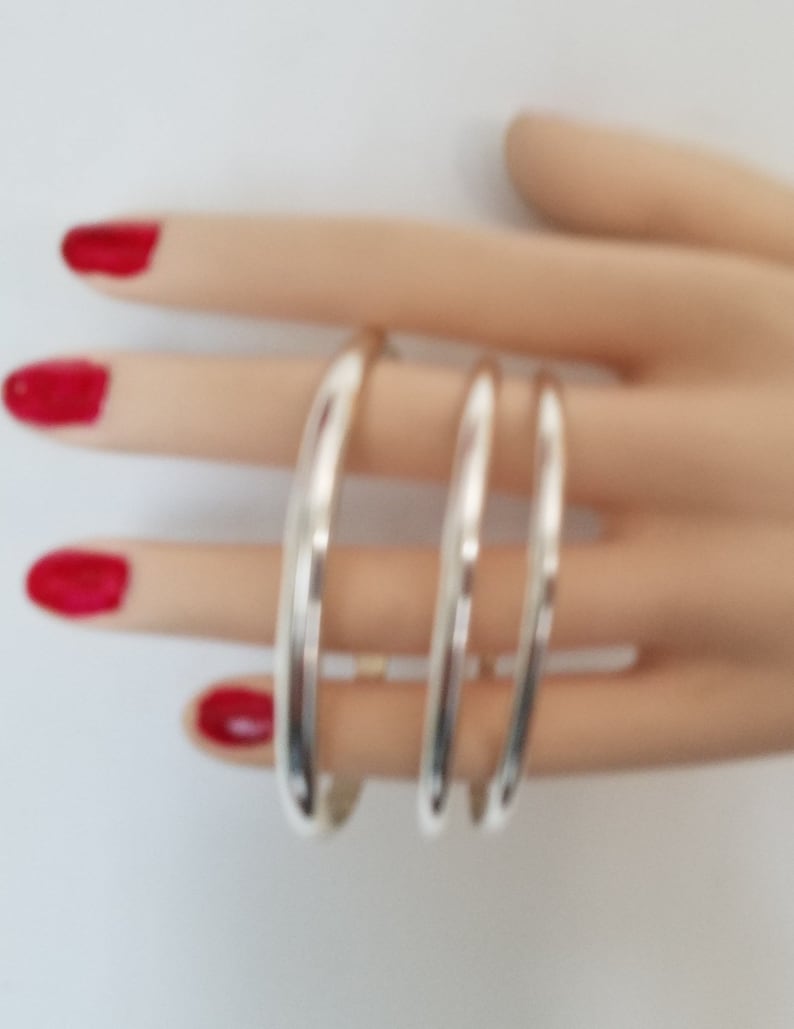 May include: Three silver bangle bracelets stacked on a hand. The bracelets are smooth and shiny.