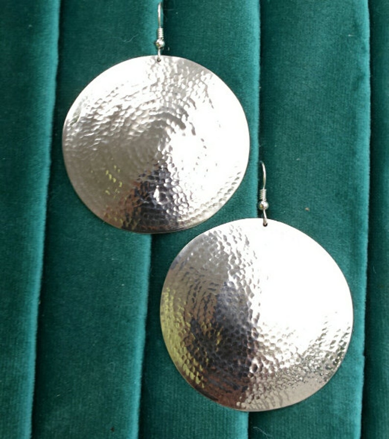May include: A pair of silver hammered disc earrings. The earrings are round and have a textured surface.
