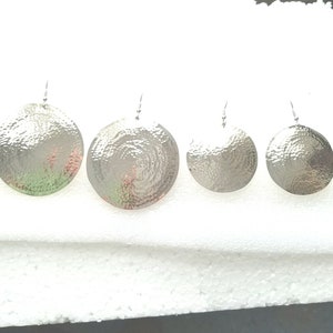 May include: Set of four silver hammered disc earrings of varying sizes. The earrings are round and have a textured surface.