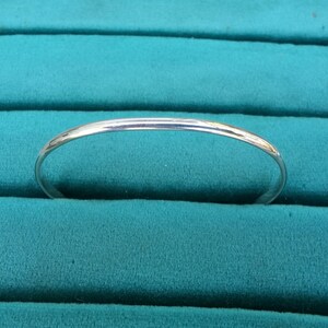 May include: A simple silver bangle bracelet, shown on a teal velvet background.