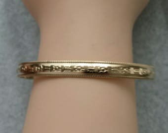 May include: A gold bangle bracelet with a delicate floral design.