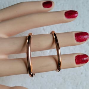 May include: Two rose gold colored metal rings, one slightly larger than the other, are worn on a finger.