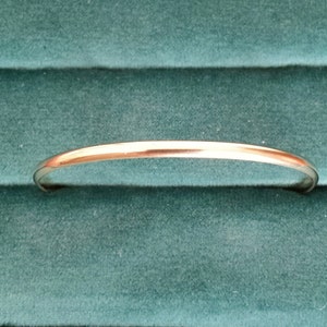 May include: A simple silver bangle bracelet, shown on a green velvet background.