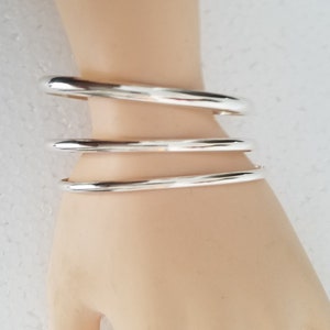 May include: Three silver bangle bracelets stacked on a model's wrist. The bracelets are smooth and shiny.